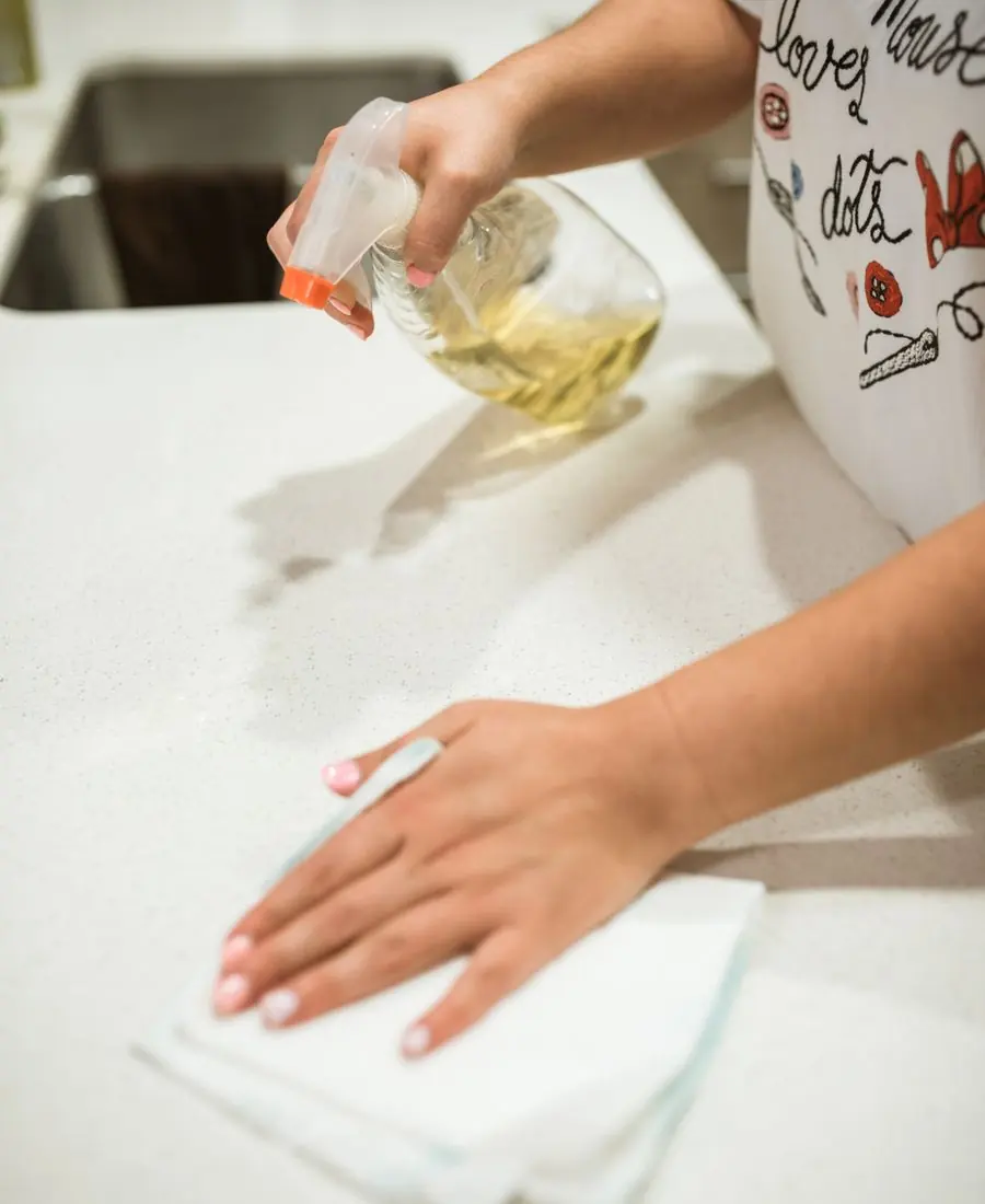 Hands wiping down a kitchen counter with a spray bottle and a cloth