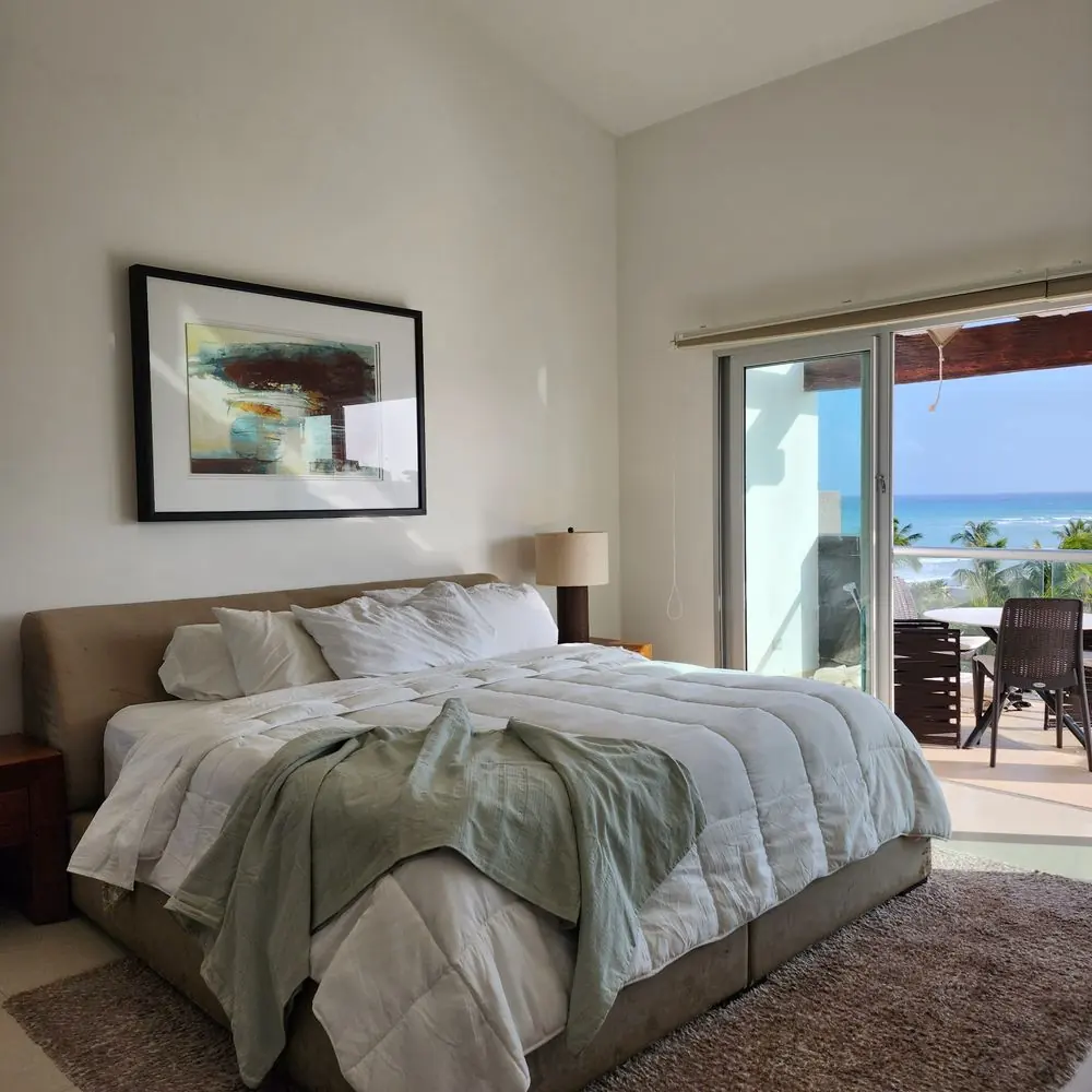 A made bed with a sage green throw in a sunlit bedroom